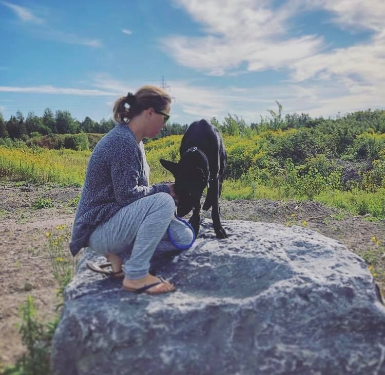 A girl sitting with a black dog on a rock.